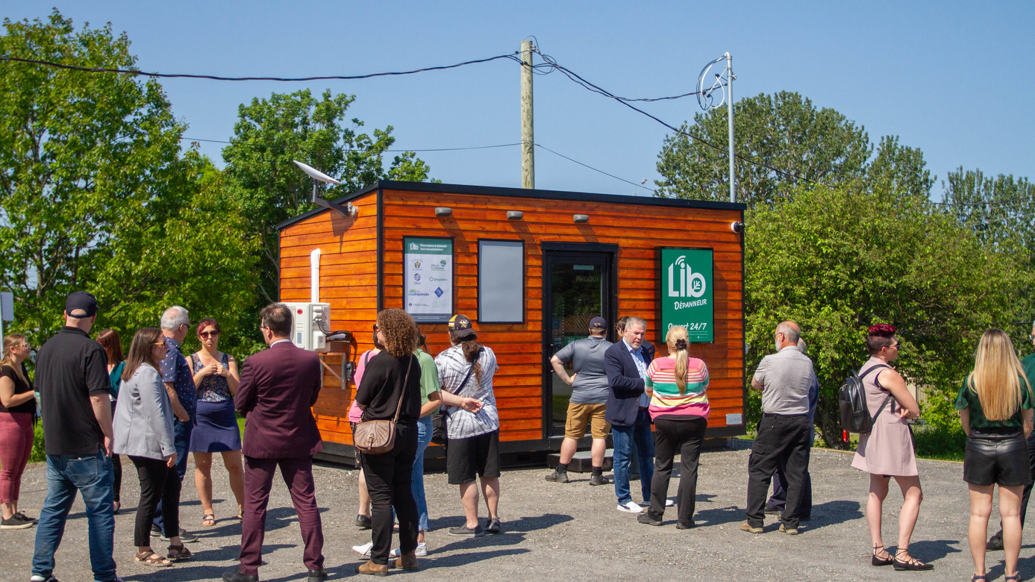 Un LIB dépanneur vue de l'extérieur, avec plusieurs personnes discutant lors d'un évènement.